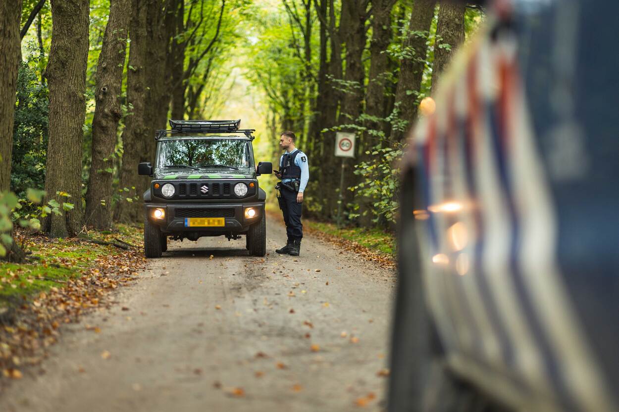 Een marechaussee spreekt in het bos een bestuurder aan.