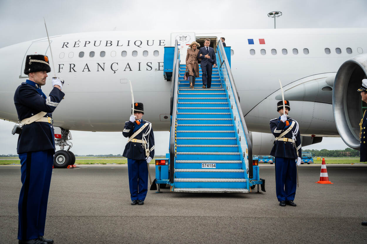 De Franse president Macron en zijn echtgenote lopen de trap van hun regeringstoestel af, opgewacht door een erewacht van de Marechaussee.
