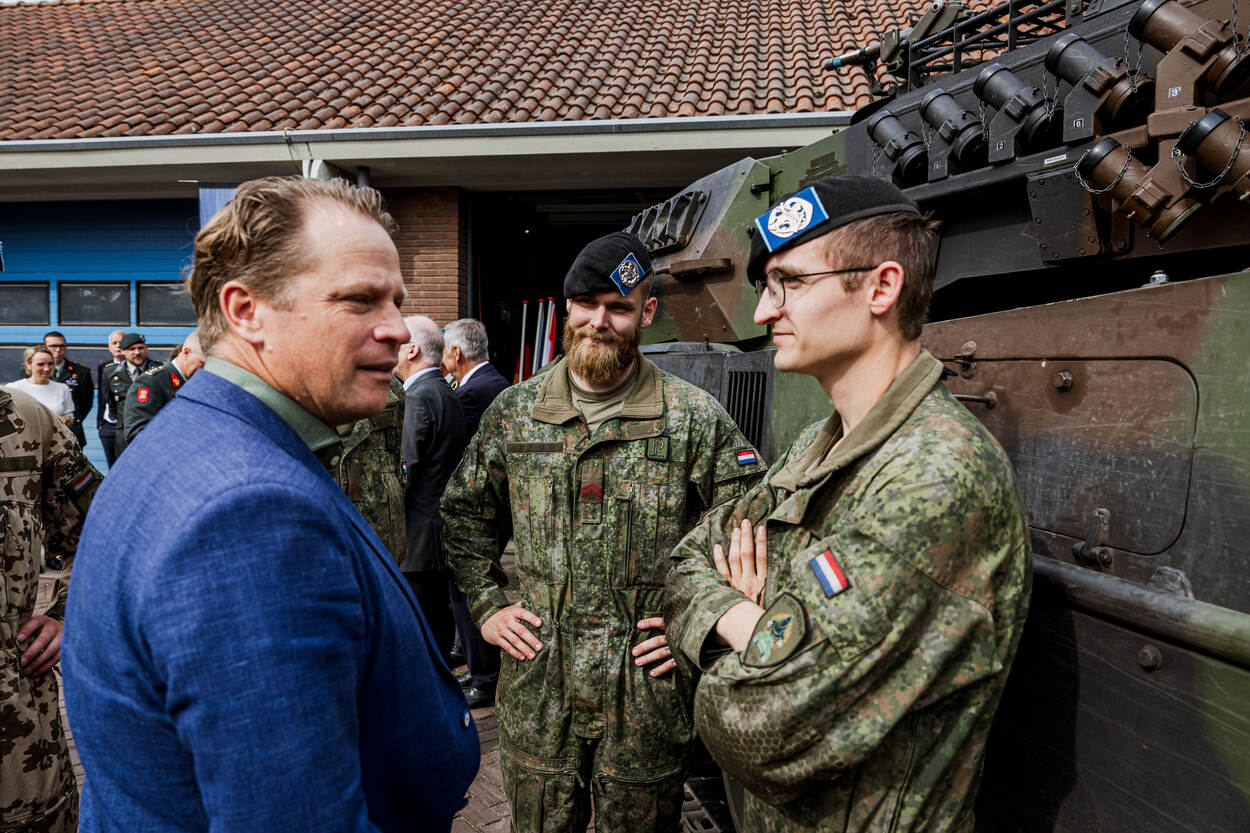 Staatssecretaris Gijs Tuinman spreekt met enkele militairen naast een tank.