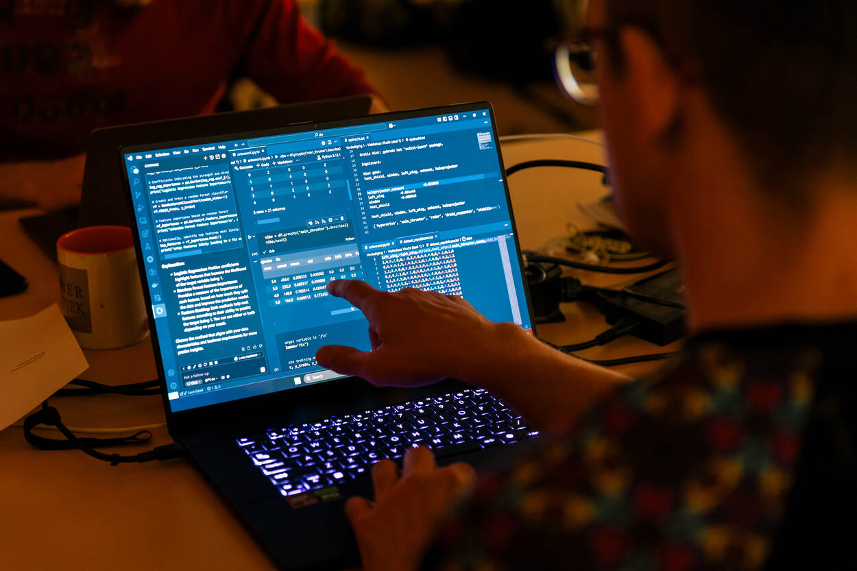 Een persoon met bril wijst iets aan op zijn laptopscherm.