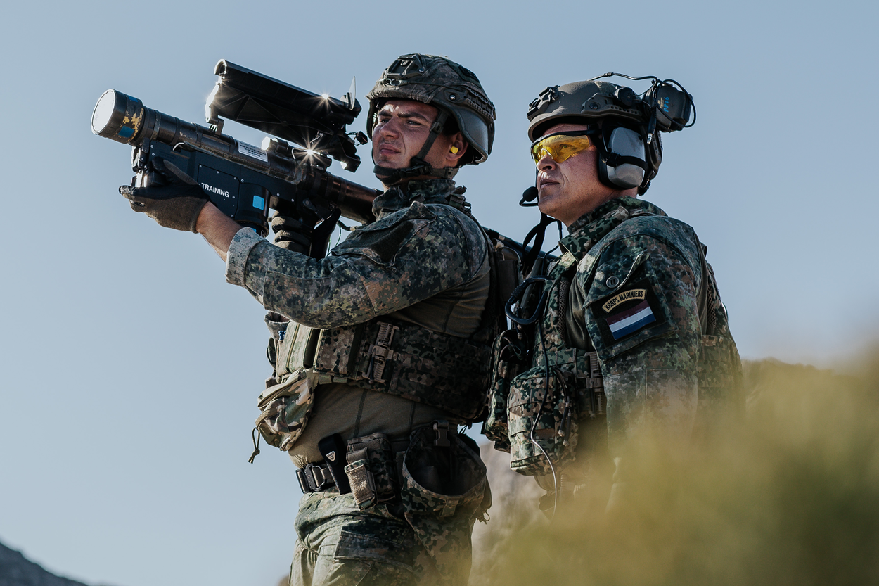 een schutter houdt een lanceerbuis vast en een instructeur begeleid hem daarbij.