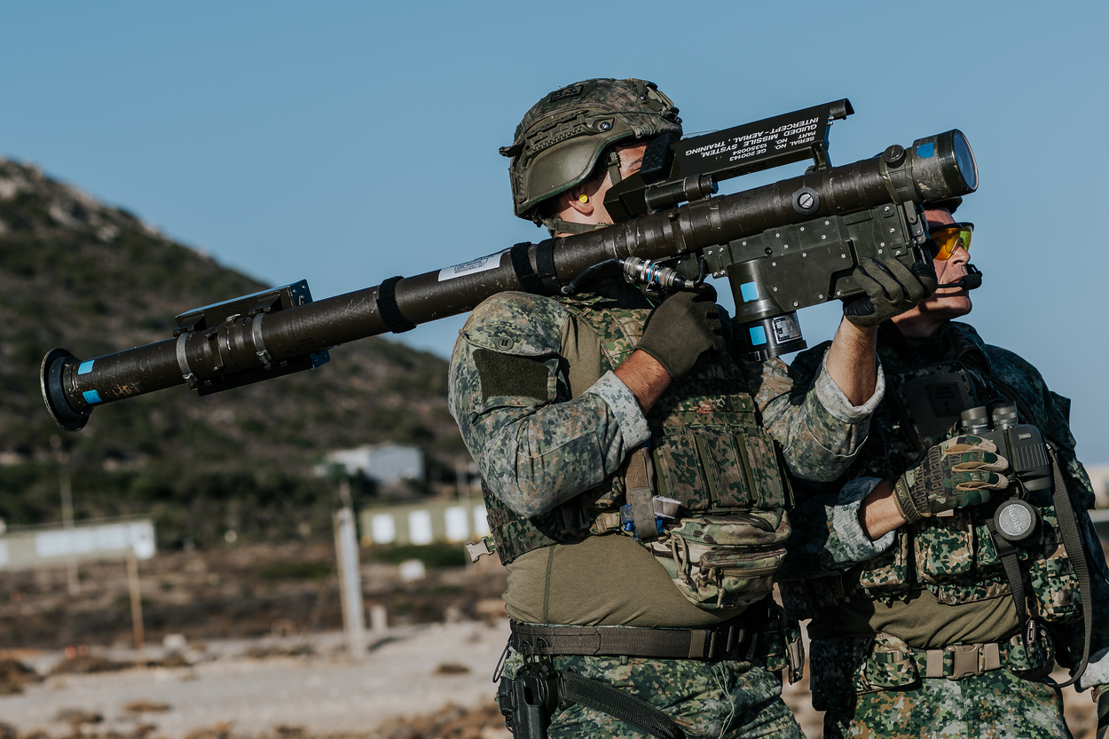 een schutter richt zijn lanceerbuis op een doel. Een instructeur kijkt mee.