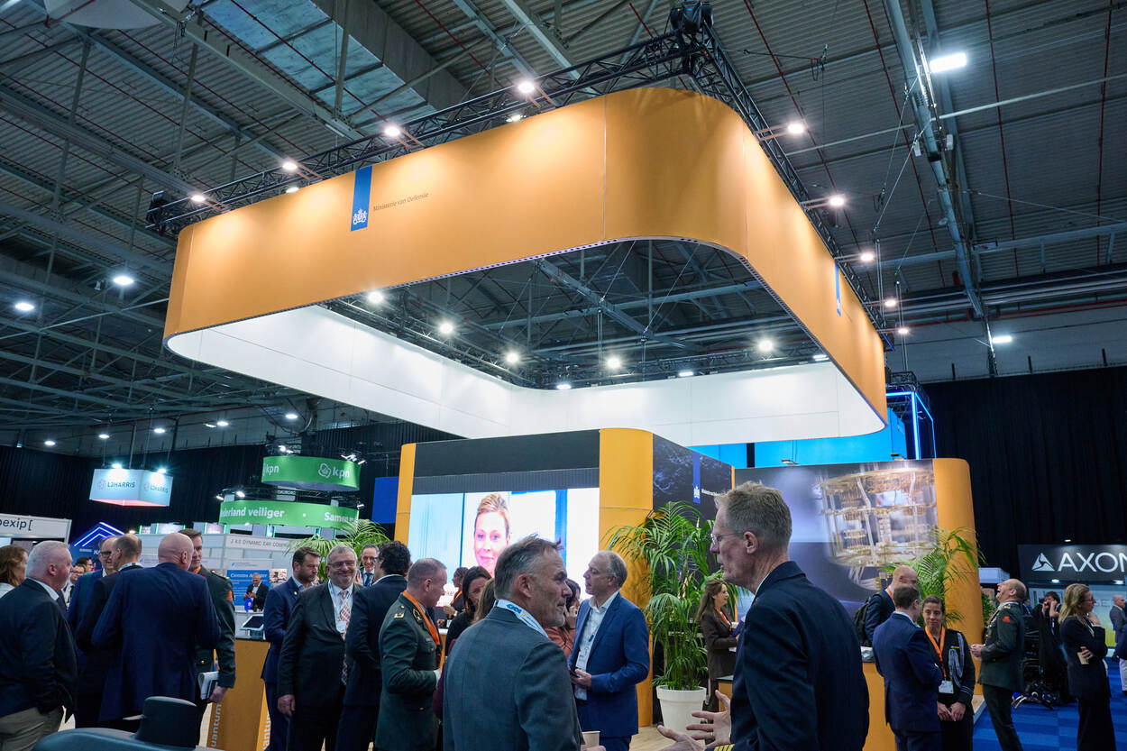 Veel mensen staan onder een groot bord met ministerie van Defensie