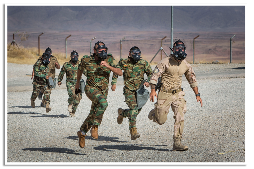 Met een Nederlandse militair voorop rennen Peshmerga met veldmasker op over een basis.