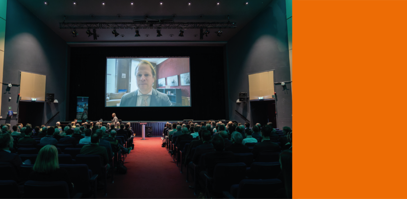 Conferentie waarbij de staatssecretaris op video te zien is.