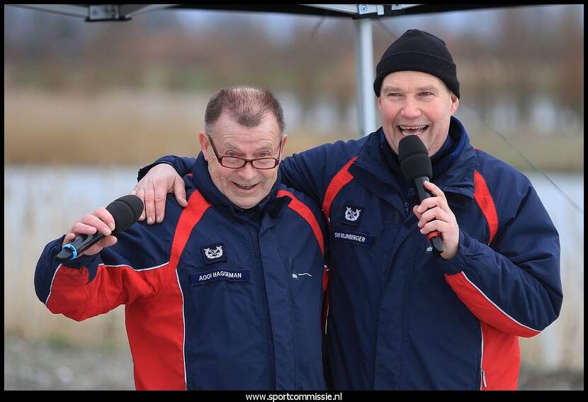 Andre Wijnberger heeft een arm om de schouder van zijn collega Bart Haggeman en houdt een microfoon onder zijn neus.