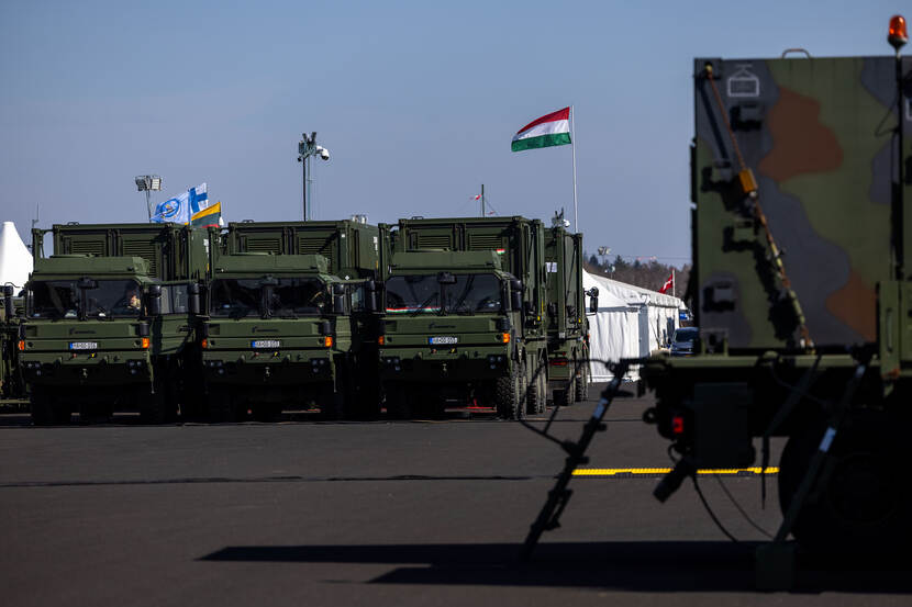 Een drietal legertrucks naast elkaar opgesteld, daarachter wappert een Hongaarse vlag.