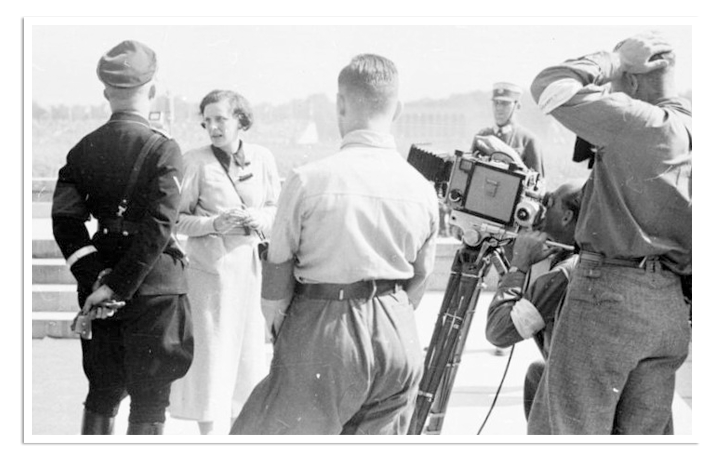 Heinricht Himmler, op de rug gezien, spreekt met Leni Riefenstahl, terwijl recht twee cameramannen toekijken.