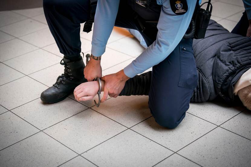Een marechaussee controleert een verdachte en slaat hem in de boeien.