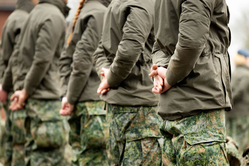 Een groep militairen gezien van de achterzijde. Hun handen hangen gevouwen achter hun rug.