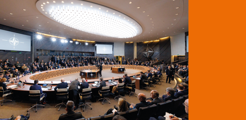 Veel personen in een vergaderruimte met in het midden een groot podium.