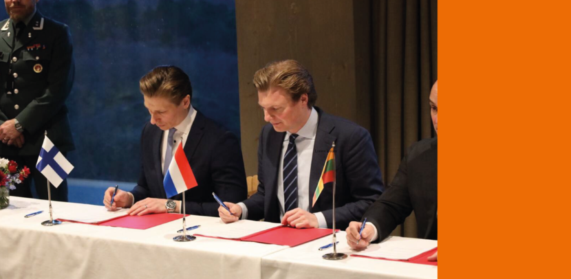 3 heren in kostuum overleggen voor een militair voertuig.