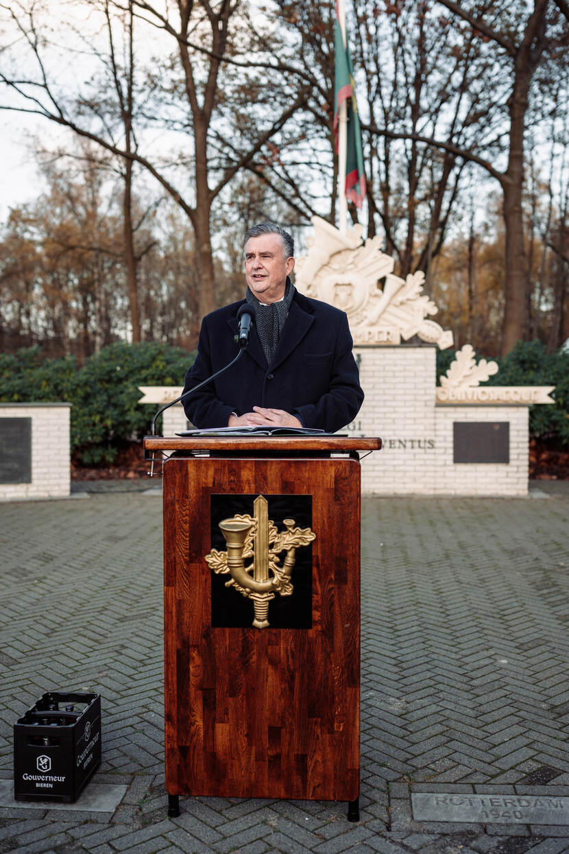 Man achter katheder houdt toespraak voor herdenkingsmonument.