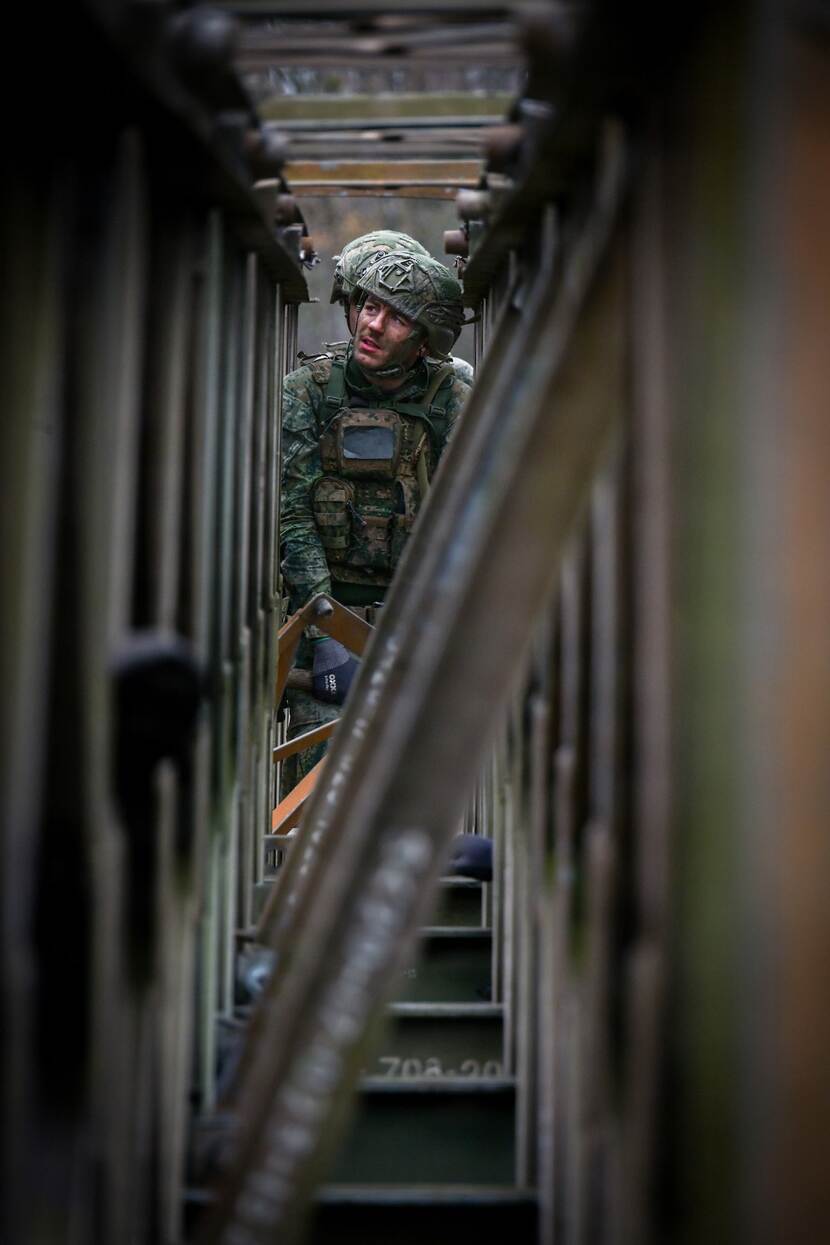 Een Nederlandse militair kijkt omhoog terwijl hij bezig is met het leggen van een brugdeel.