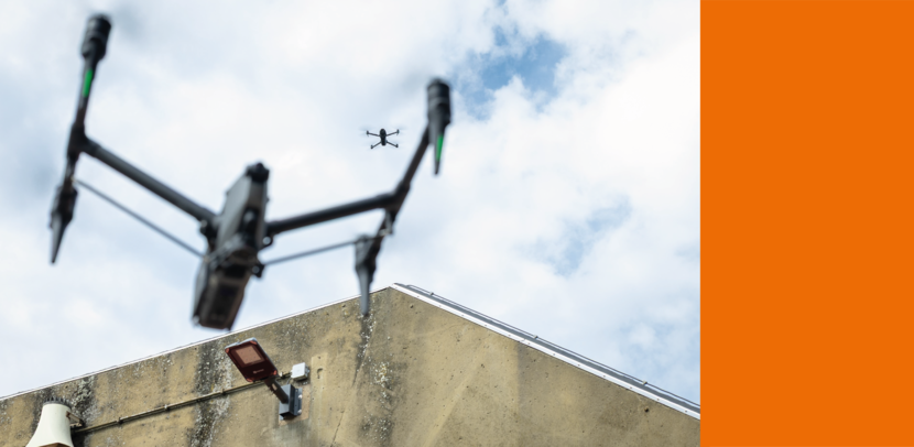 Twee drones hangen stil boven een hangaar.