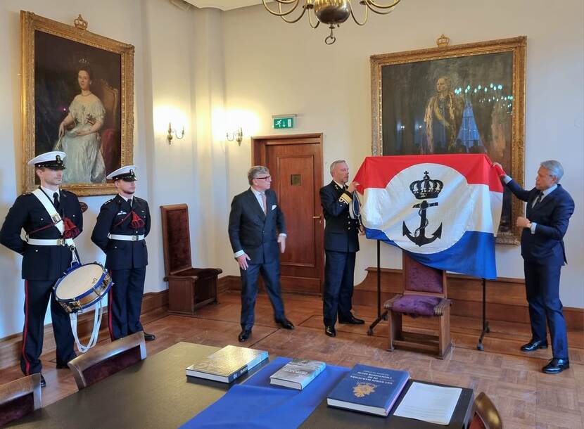 Twee muzikanten van de Tamboers en Pijpers van het Korps Mariniers staan naast de litho, die wordt onthuld door luitenant-admiraal Bauer en Jan Jaap van Weering.