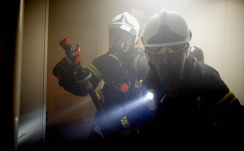 Twee marinemensen in hittewerende pakken te midden van veel rook.