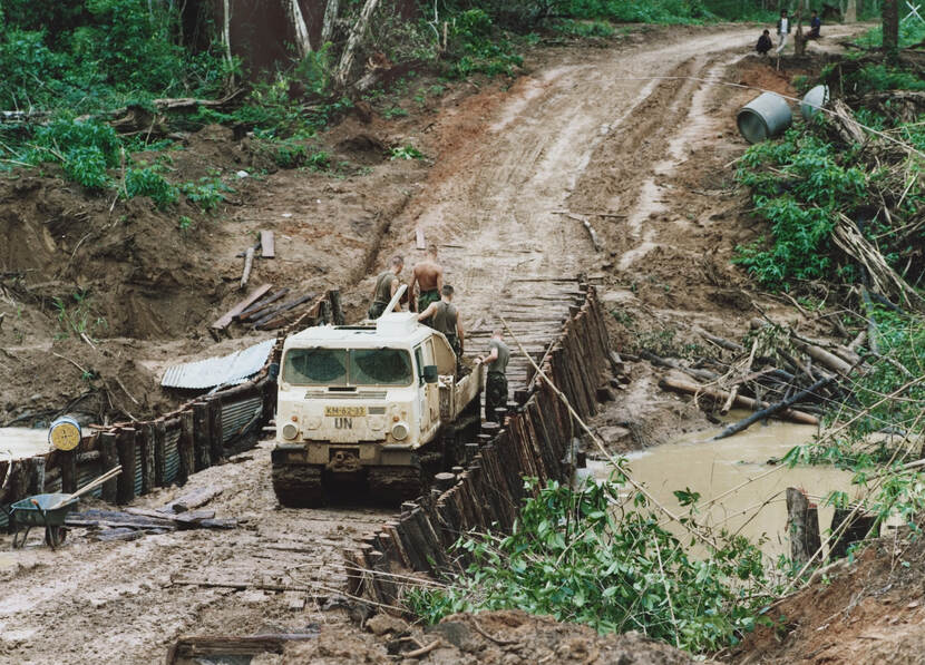 Een rupsvoertuig met UN-opschrift staat op een provisorische brug ergens in Combodja.