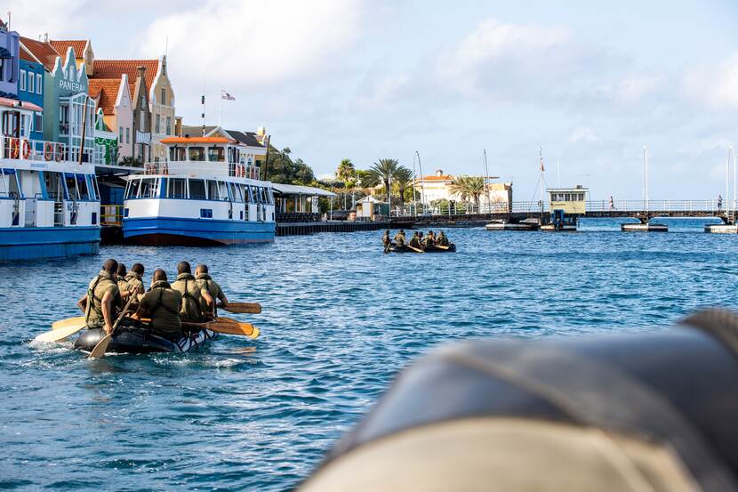EMV’ers die met rubberboten de kade van Willemstad voorbij peddelen.