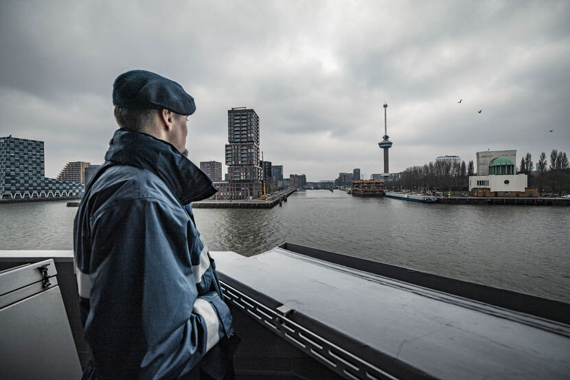 Een collega van de marine kijkt richting de kade, waarop in de verte de Euromast te zien is.