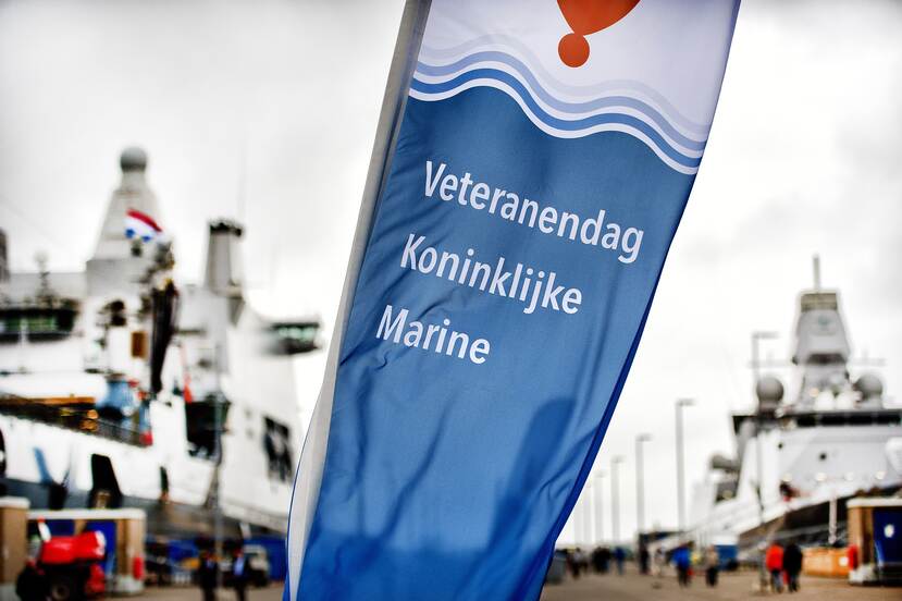 Schepen aan de kade op de achtergrond. Op de voorgrond de vlag van de Veteranendag Koninklijke Marine.