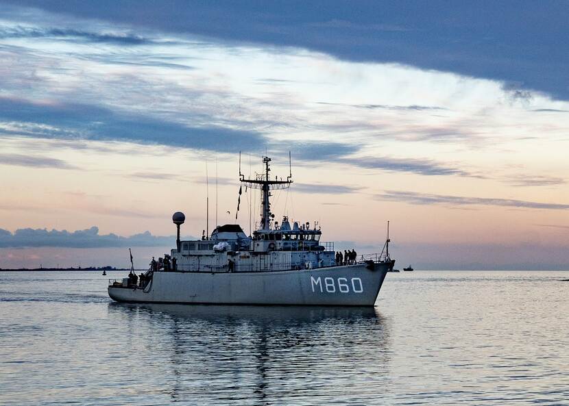 Zr.Ms. Schiedam bij ondergaande zon bij de ingang van een haven.