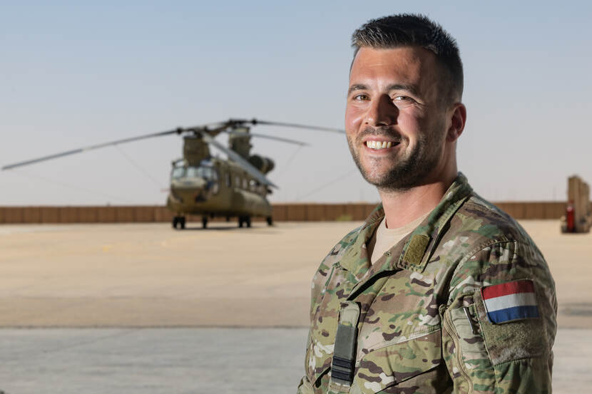 Kapitein Frank kijkt in de lens van de camera, met op de achtergrond een Chinook.