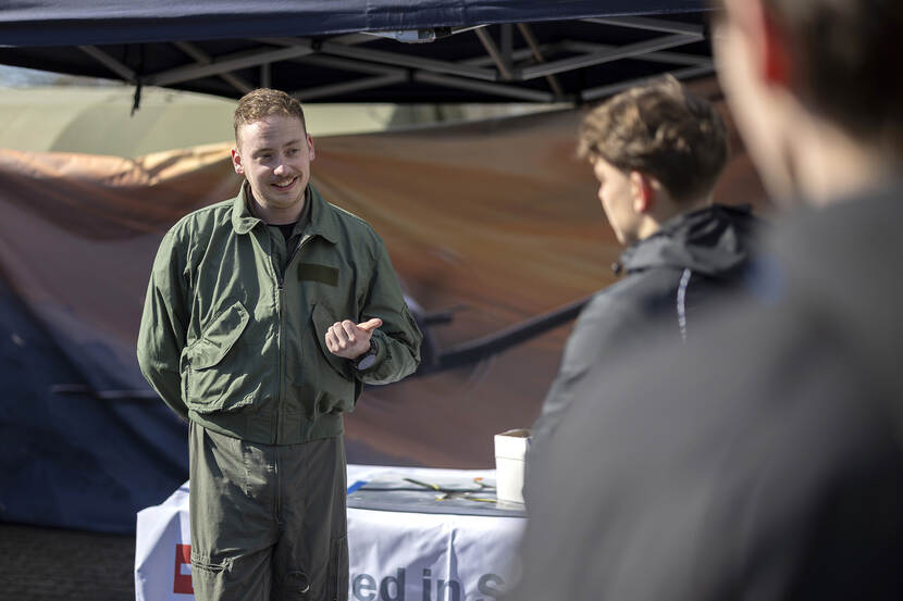 Een vlieger in vliegeroverall spreekt een groep jongeren toe bij zijn informatiestand.