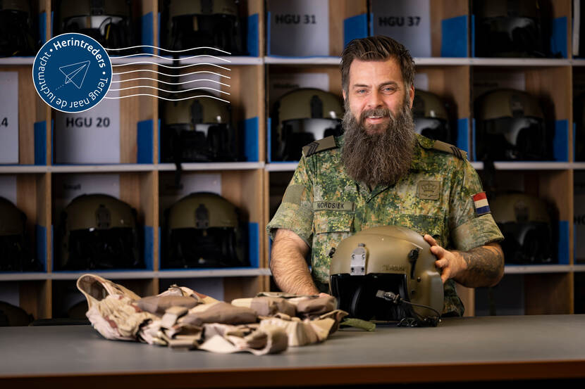 Sergeant Einar Nordsiek poseert achter een tafel met daarop een vliegerhelm en -vest. Achter hem een vakkenkast met vliegerhelmen.