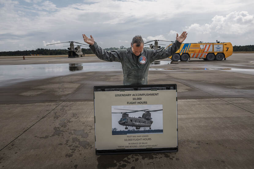 Jaap Lokker met een bord waarop een Chinook en de woorden 10.000 flight hours staat. Op de achtergrond twee Chinooks en een bluswagen.