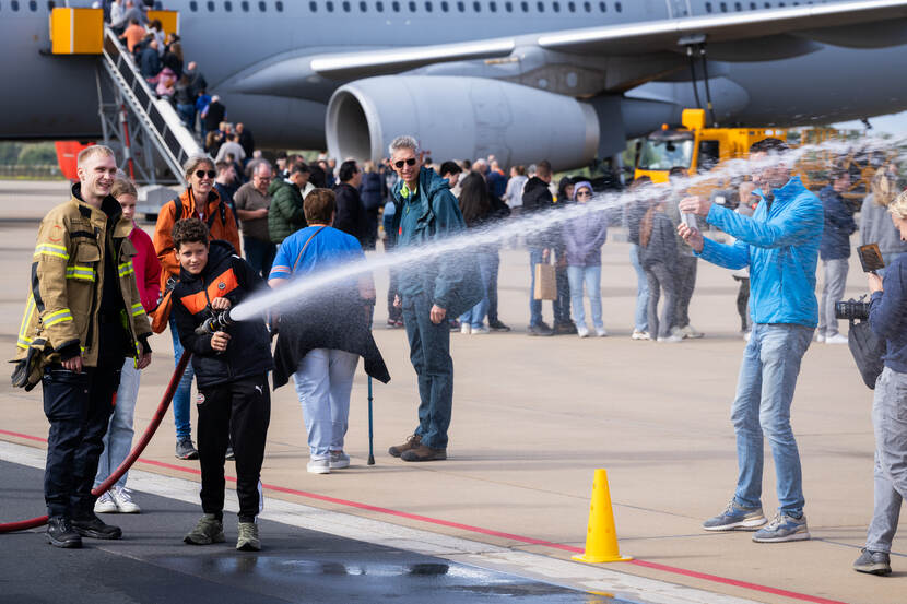 Bezoeker spuit met een brandweerslang, op de achtergrond een rij bij een tankvliegtuig.