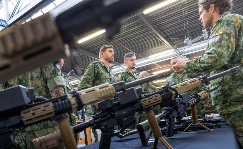 Staande geweren op een tafel met militairen eromheen.