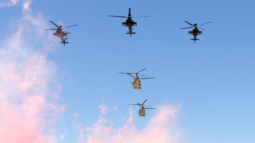 Vijf overvliegende helikopters tegen een blauwe lucht.