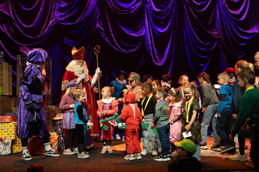 Sinterklaas en Pieten samen met jonge kinderen op een podium met pakjes.