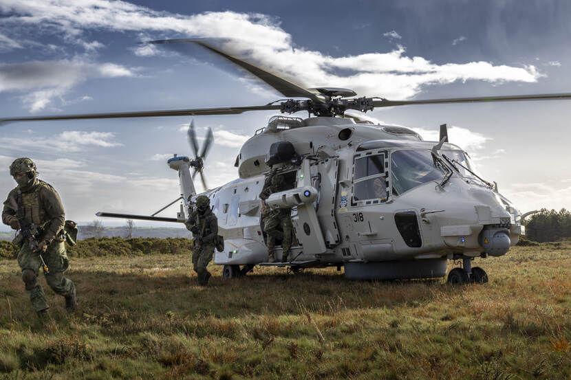 Mariniers lopen en rennen uit een op gras gelande NH90.