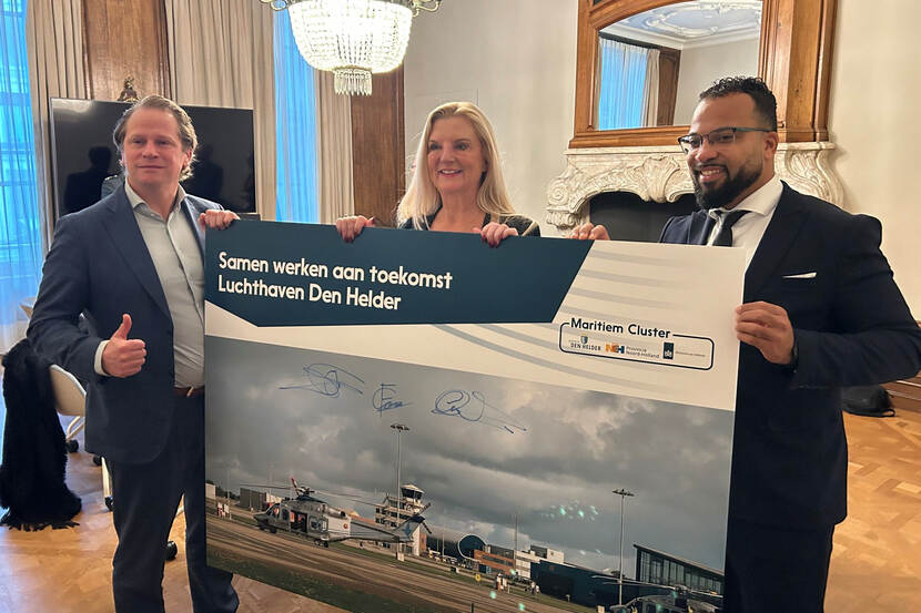 Tuinman houdt samen met twee andere mensen een bord vast met daarop een foto van Luchthaven Den Helder en de tekst ‘Samen werken aan toekomst Luchthaven Den Helder’. Op het bord staan drie handtekeningen.