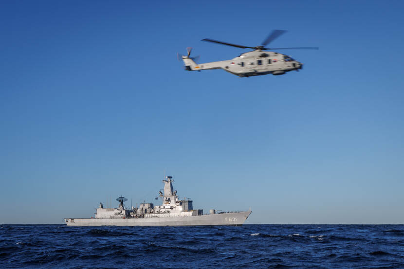 Zr.Ms. Van Amstel vaart door de Oostzee, rechtsboven het schip vliegt de NH90 boordhelikopter.