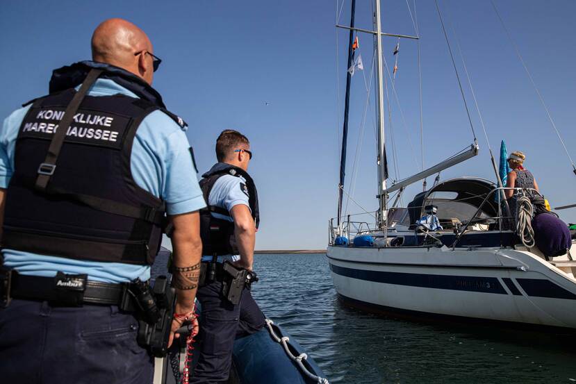 2 marechaussees controleren vanaf een vaartuig een ander vaartuig.