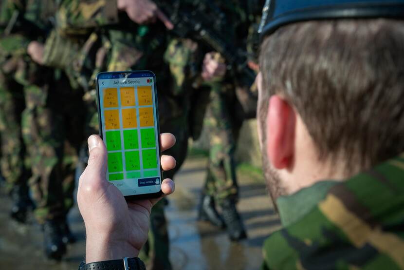 Instructeur houdt een smartphone in beeld waarop in kleurenschema’s is te zien wat de status is van elk individu.