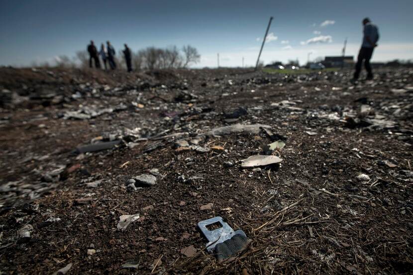 Op een donker veld ligt een onderdeel van een stoelriem. Op de achtergrond mensen op de crashsite.