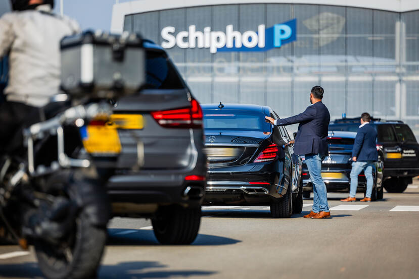 Persoonsbeveiligers staan op Schiphol naast de auto’s die in konvooi rijden.