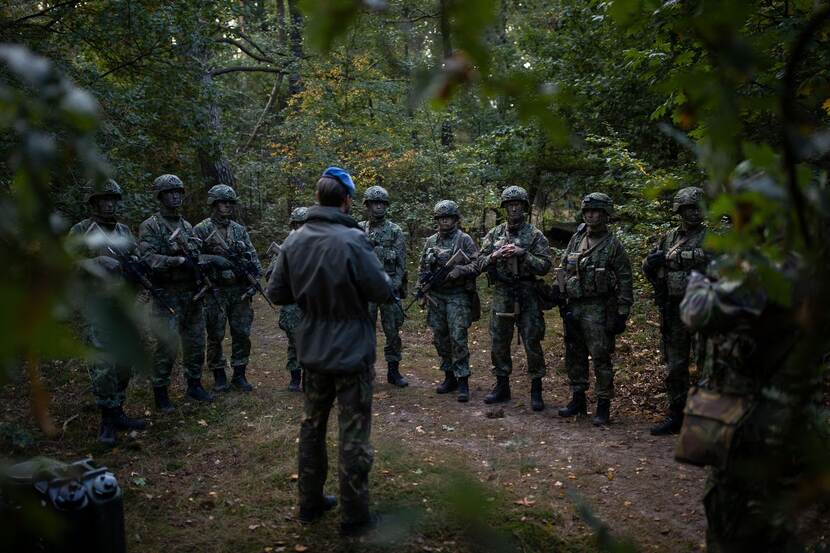 Marechaussees in opleiding krijgen instructie in het bos. Ze dragen camouflagekleding.
