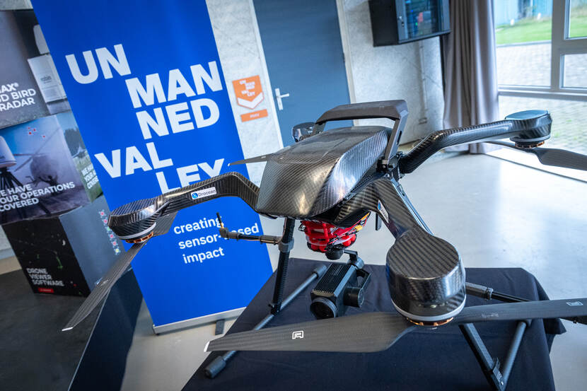 Een donkergrijze drone staat op een tafel, daarachter blauwe banners met de tekst ‘Unmanned Valley’.