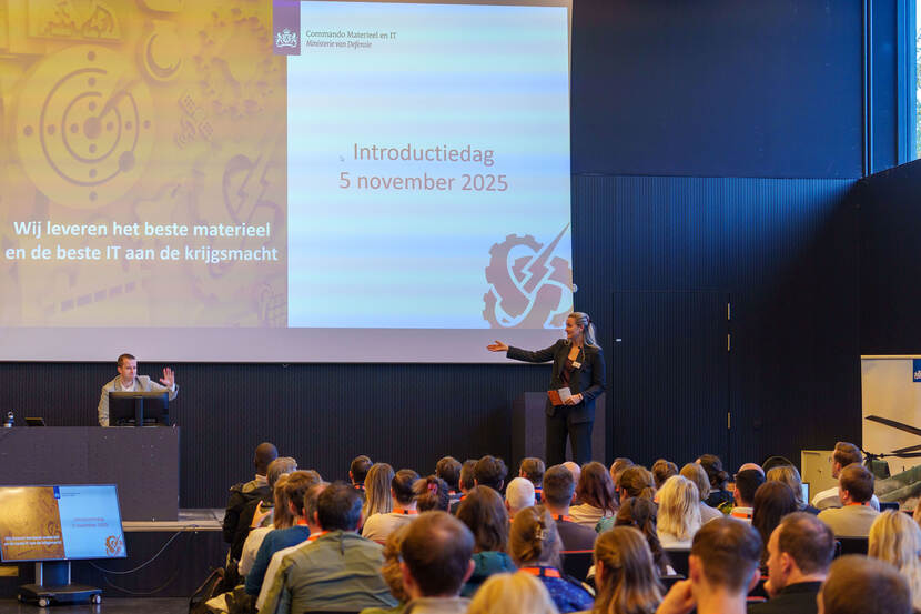 Een presentatie tijdens de Introdutiedag 5 november 2025 over het leveren van het beste materieel en IT aan de krijgsmacht, met twee sprekers en een publiek in een zaal.