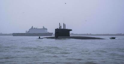 Onderzeeboot half boven water met op de achtergrond een marineschip.