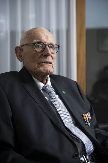 Bert Carper in een stoel met een blauwe stropdas voor en donkerblauw colbertjasje.