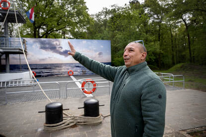 Leenhouwers geeft uitleg over het marinegedeelte van het oefengebouw, terwijl hij buiten voor een nagebouwd helikopterdek staat.