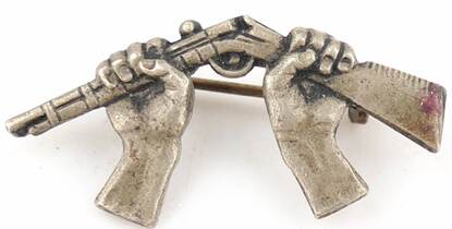 Een speldje van twee handen die een geweer breken. Het symbool van de pacifistische beweging begin vorige eeuw.