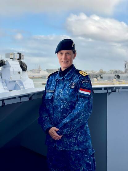 Commandant in uniform staat buiten op het dek van haar marineschip
