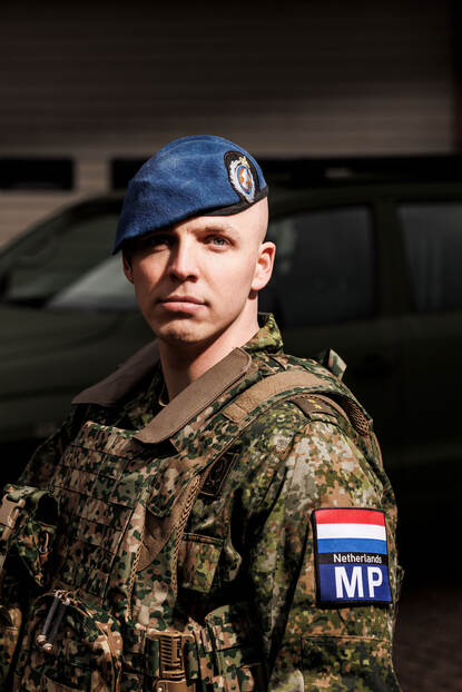 Portretfoto van luitenant Gijs met blauwe baret op en armpatches van de Militaire Politie en een Nederlandse vlag.